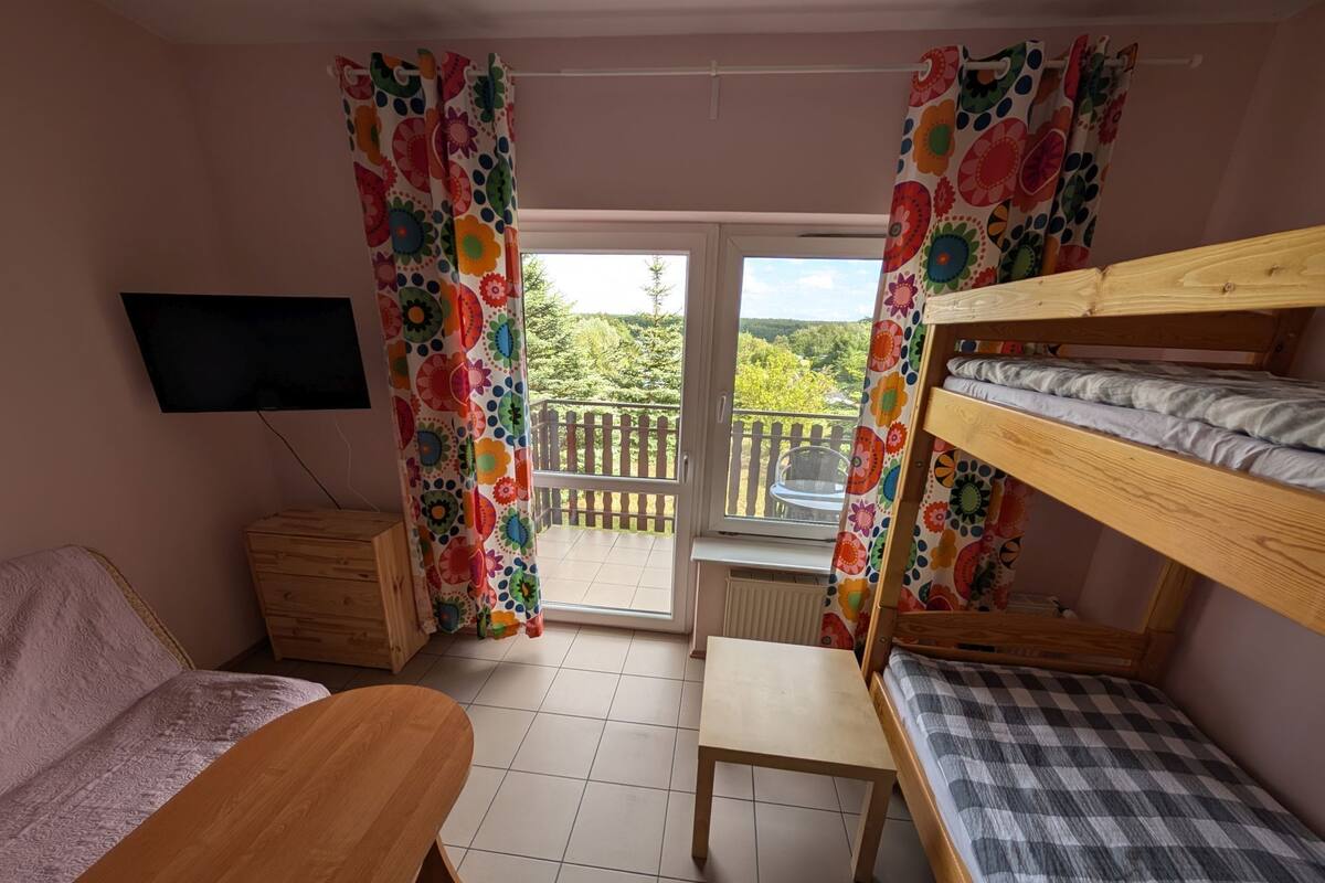 A room with a bunk bed, a desk, a chair, a television, and a window with curtains.