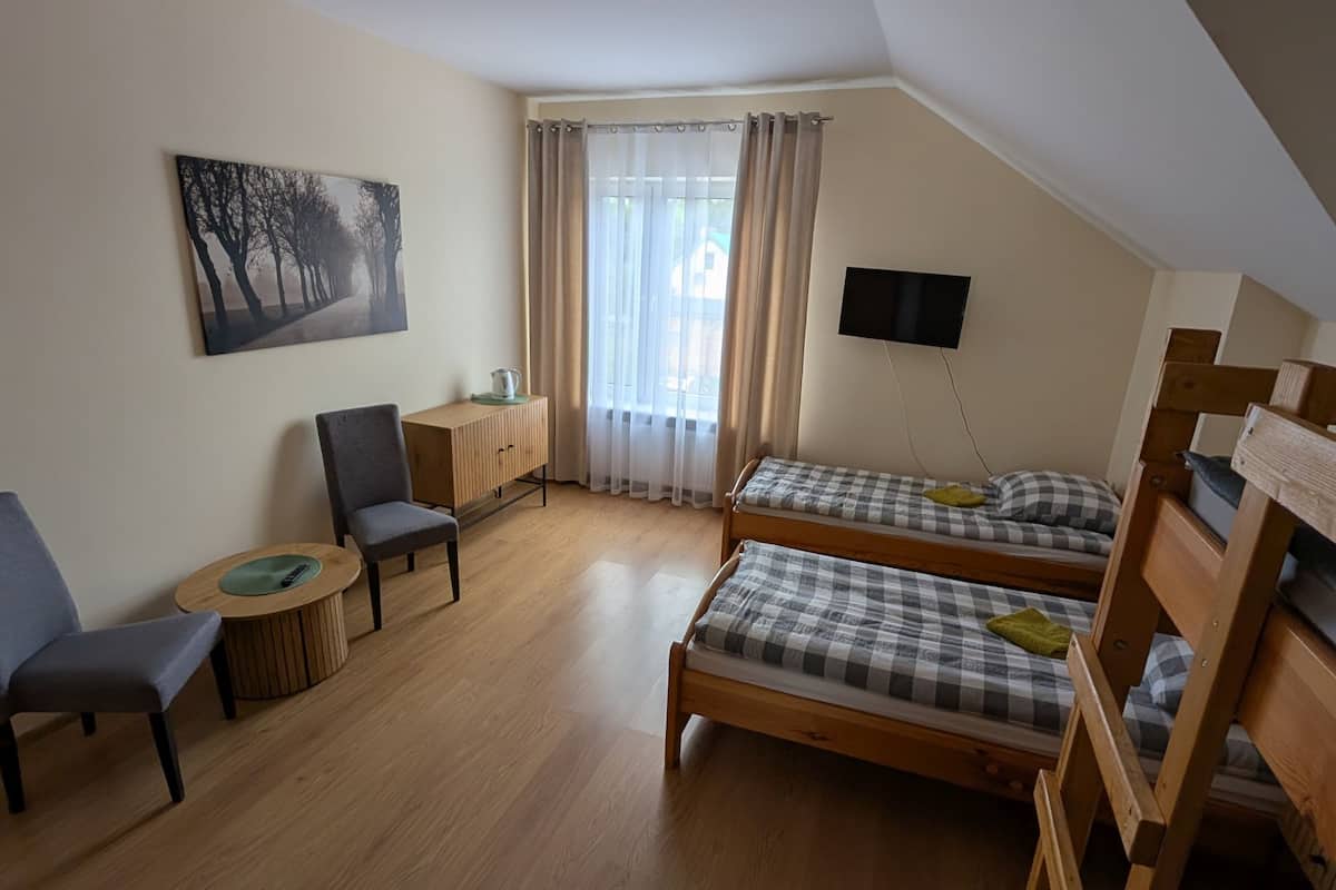 A room with two wooden bunk beds, a desk with a chair, a small table, a painting on the wall, and a TV mounted on the wall.