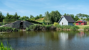 A rustic stone bridge over a calm pond, a small white building, and a red structure with a porch. - Zatoka Zabłockich Ośrodek Wypoczynkowy (Znin)