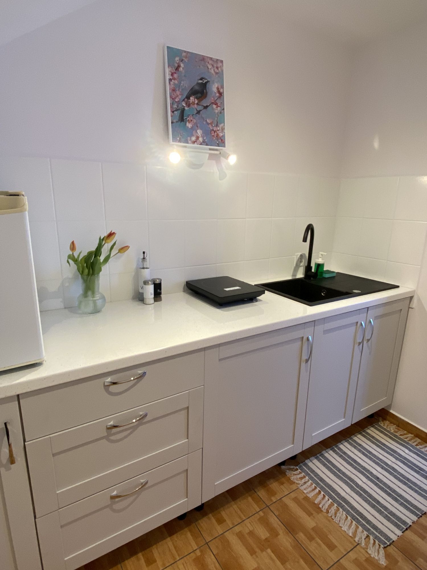A modern kitchen with white cabinets, a black countertop, a sink, and a small vase with flowers.