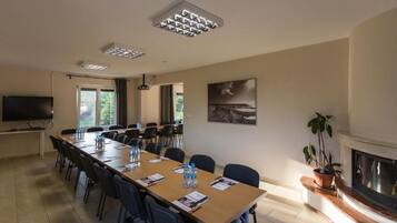 A conference room with a long table, chairs, a flat-screen TV, a fireplace, and a painting on the wall.