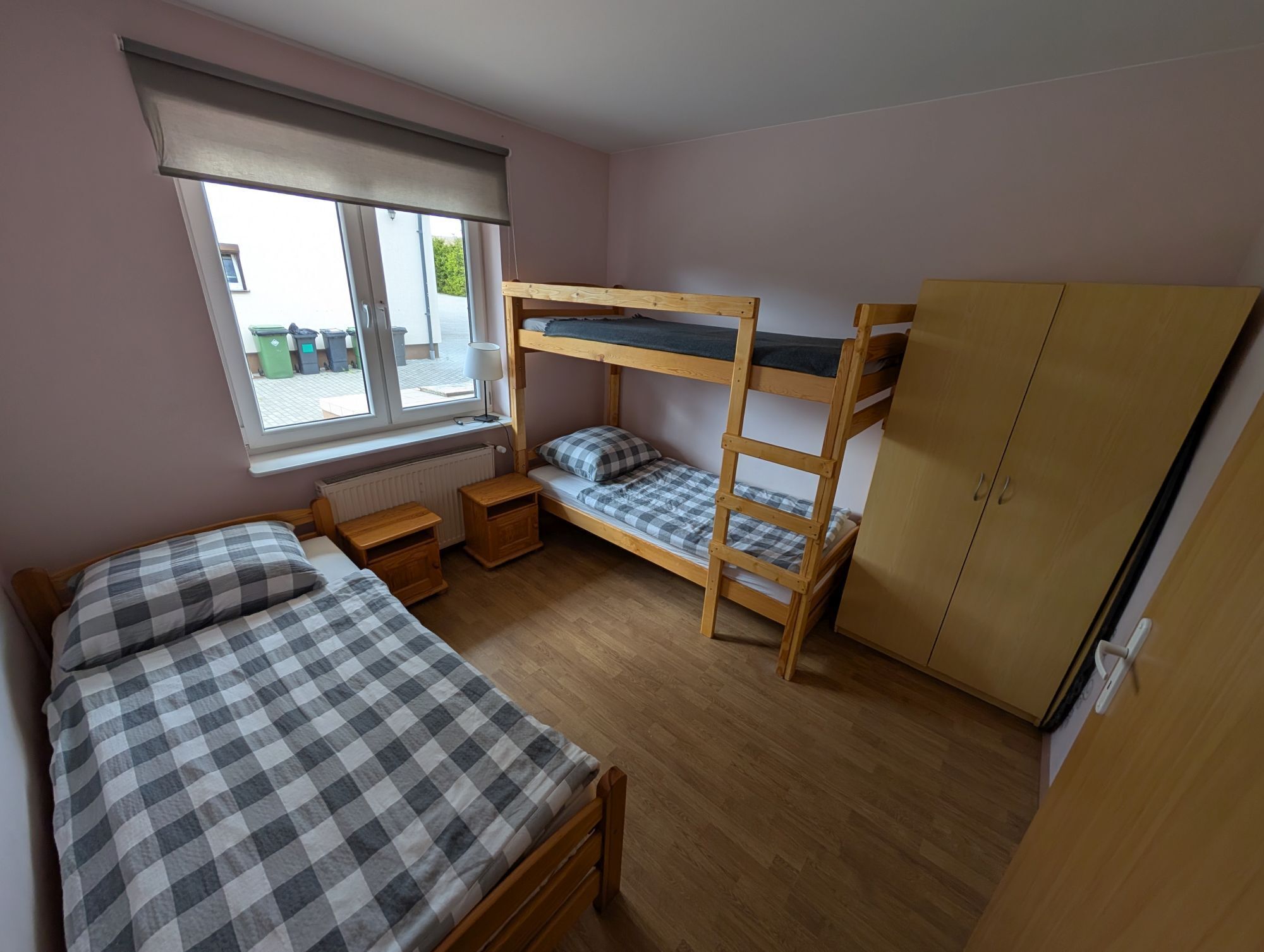 Et soveværelse med køjeseng, en enkeltseng, et træskab, et vindue med persienner og en radiator.