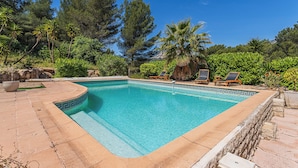 A rectangular pool with a geometric tile border, surrounded by a stone deck and lush greenery, including palm trees and dense foliage. - Villa de L'Uba - Welkeys (Toulon)