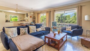 A spacious living room with a dark blue sofa set, a wooden coffee table, and a view of a balcony with a scenic landscape. - Villa de L'Uba - Welkeys (Toulon)
