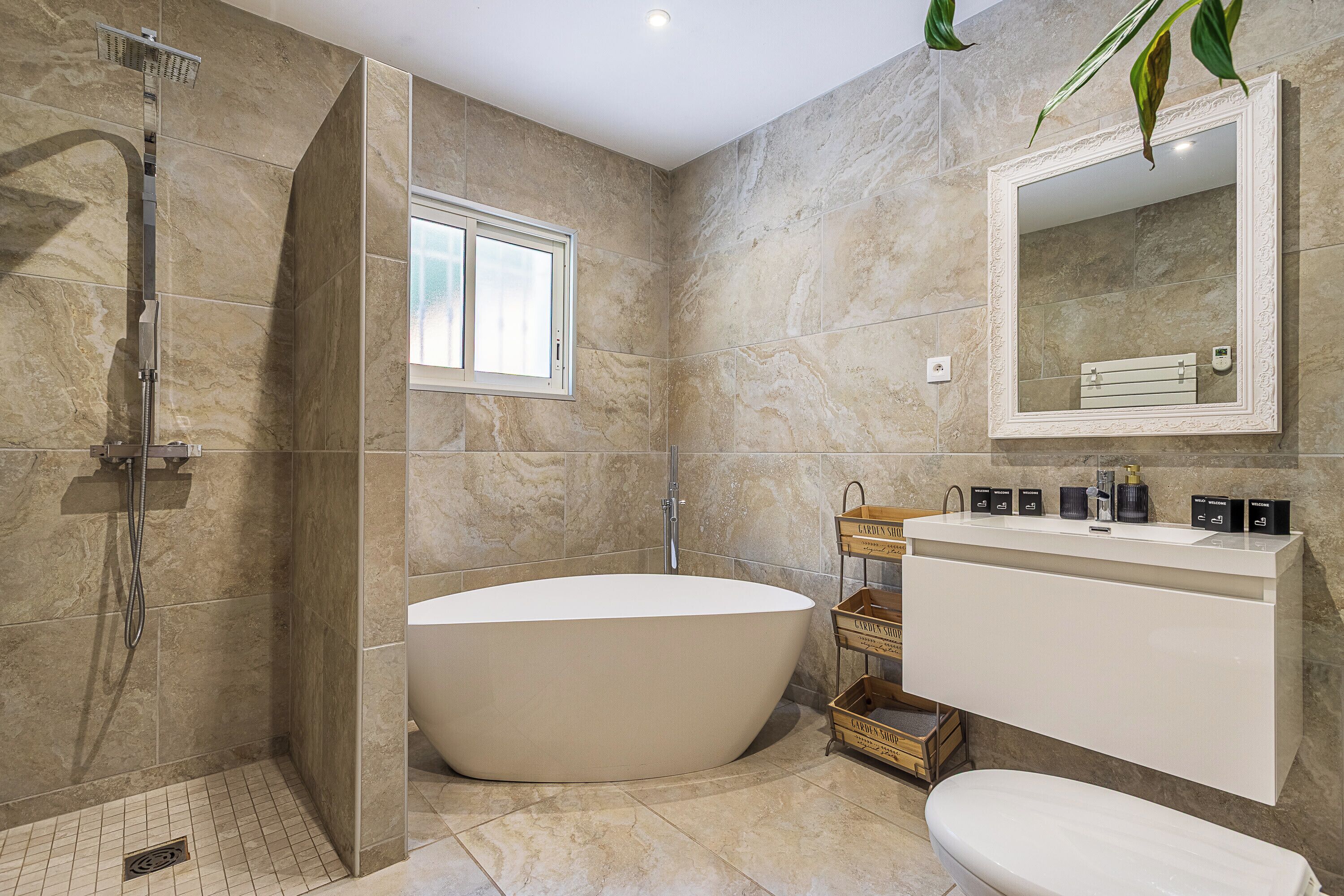 A modern bathroom with a freestanding bathtub, a walk-in shower, a vanity with a mirror, and a window providing natural light.