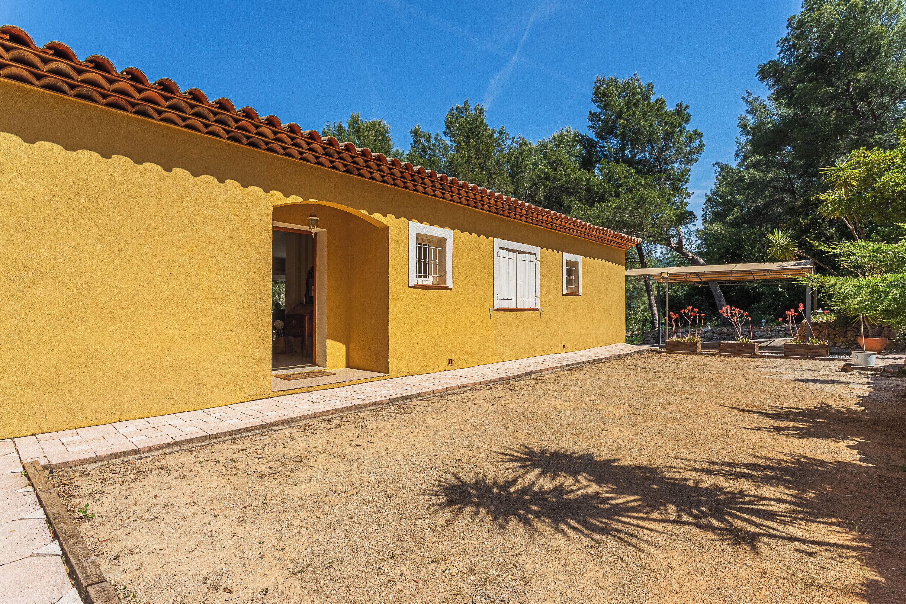 Un bâtiment jaune avec un toit en tuiles, un patio couvert et une cour en terre battue.