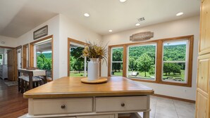 A kitchen with a large island, wooden cabinets, and a view of a lush green landscape through large windows.