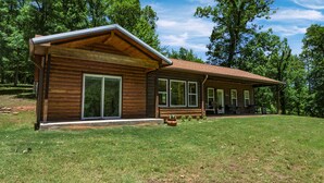 A wooden cabin with a large sliding glass door, a covered porch, and a well-maintained lawn.
