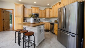 A modern kitchen with wooden cabinets, a stainless steel refrigerator, and a central island with stools.
