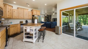 A modern kitchen with wooden cabinets, a central island with stools, and a sliding glass door leading to an outdoor patio area.