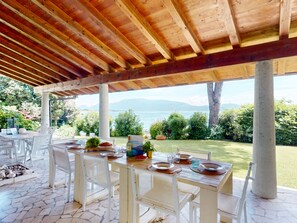 A covered outdoor dining area with a view of the sea and mountains. - Villa 7 Bello by Bookinggardalake (Manerba del Garda)