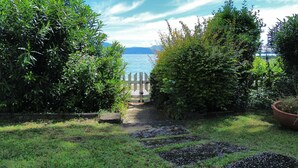 Ein Gartenweg führt zu einem Tor mit Blick auf einen See und Berge in der Ferne.
