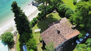 Luftaufnahme eines Küstengrundstücks mit einem Haus mit Ziegeldach, einem Strand und umgebender Vegetation.