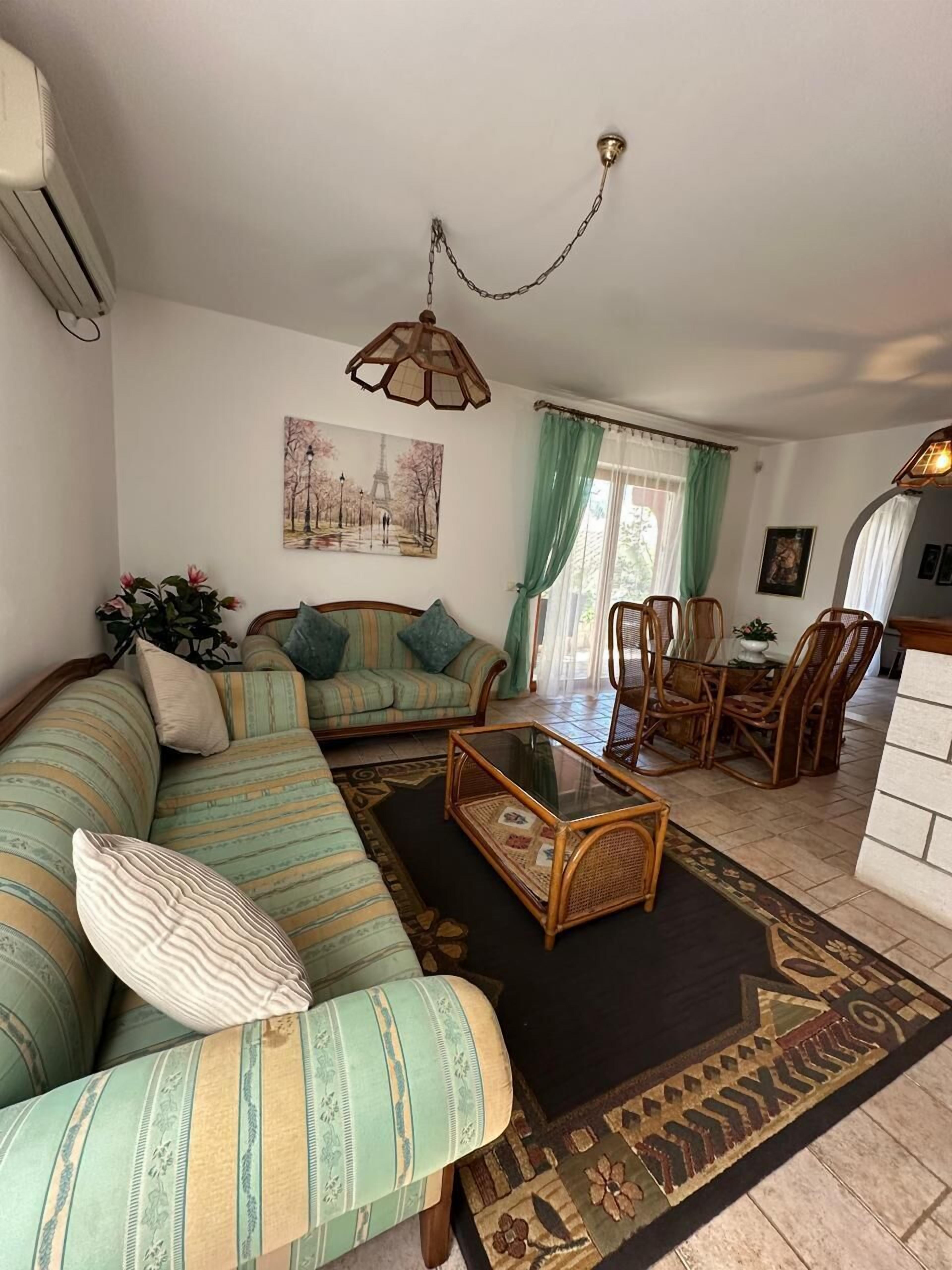 Un salon comprenant un canapé, une table basse, une table à manger avec des chaises, un luminaire suspendu et un tableau accroché au mur.