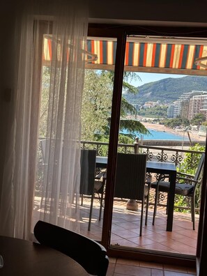 A balcony with a table and chairs, a view of a beach, and a mountainous landscape.