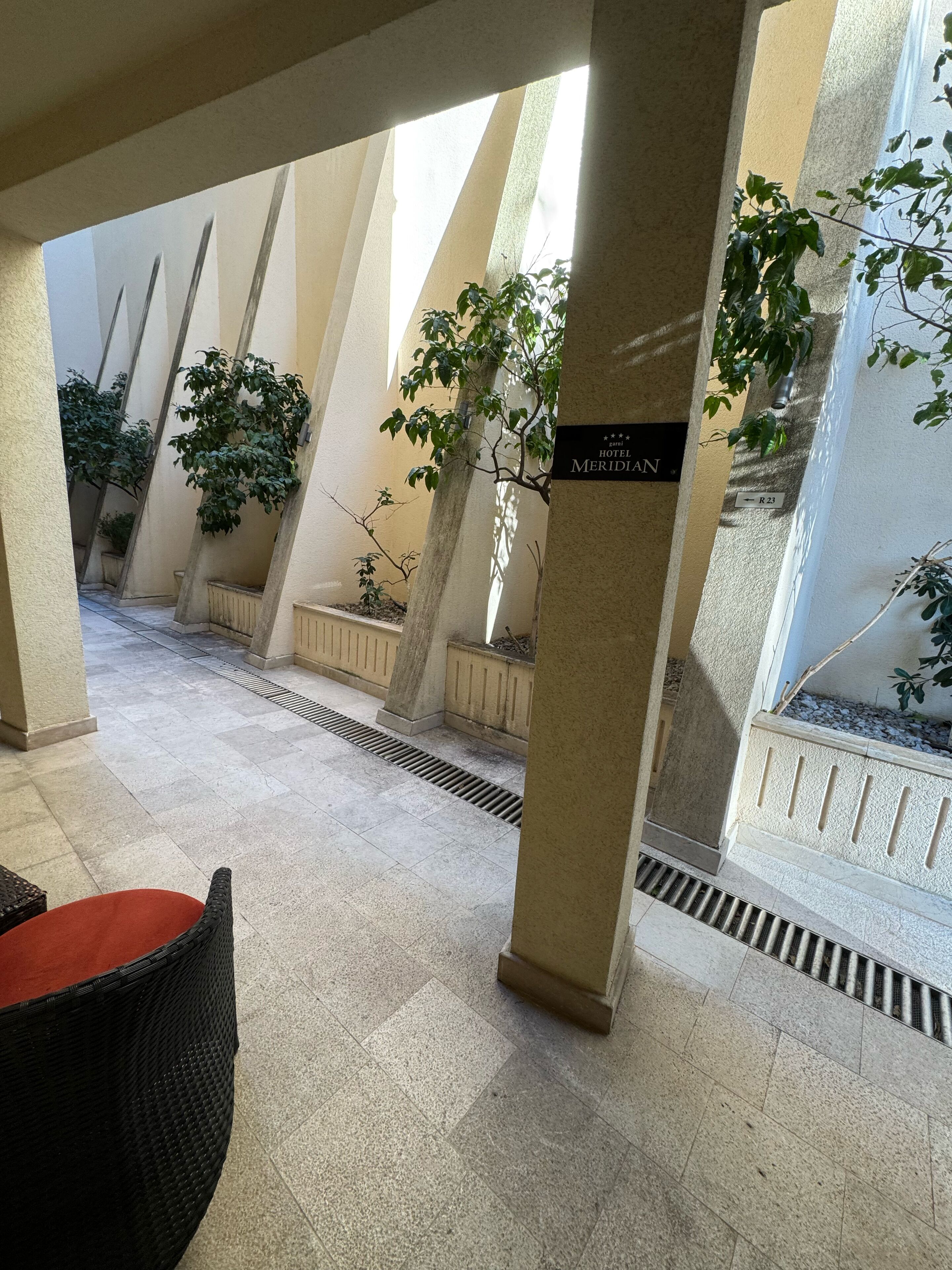 Un pasillo de hotel con suelo de baldosas, columnas y plantas en macetas.