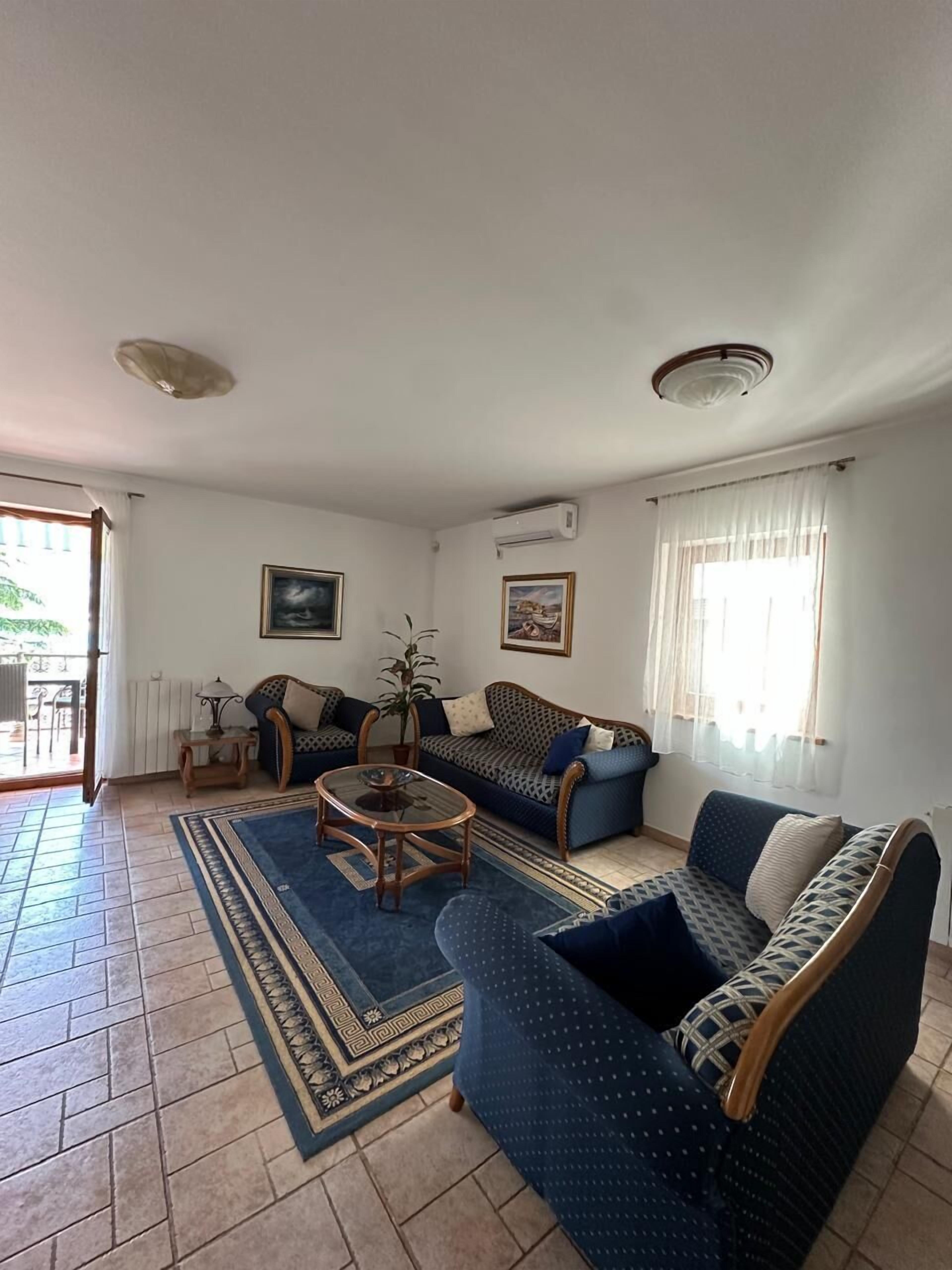 Ein Wohnzimmer mit einer Couch, Sesseln, einem Couchtisch und einem gemusterten Teppich.