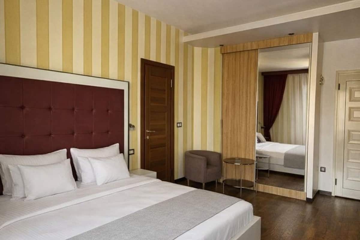 Quarto de hotel com uma cama grande, uma mesa pequena, uma cadeira e uma área de dormir separada com uma cama.