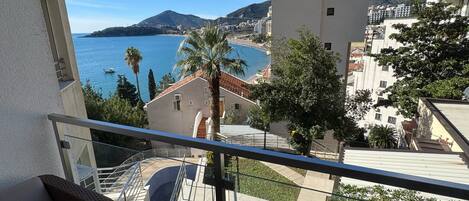 A balcony with wicker furniture, a view of a coastal area, and a building with a tiled roof.