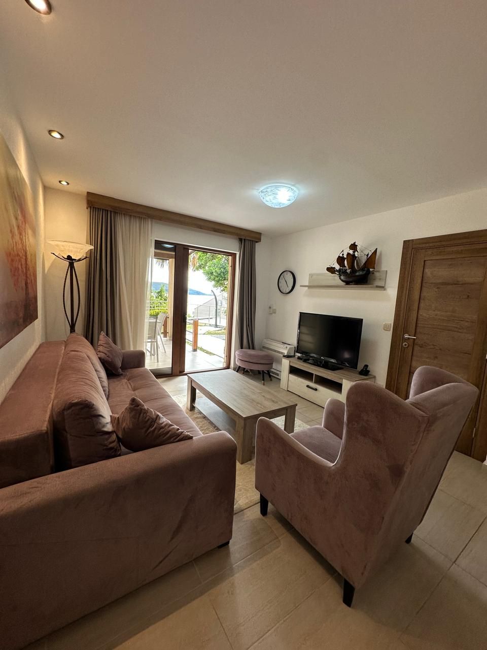 A living room with a sofa, armchairs, a coffee table, a TV, and a door.