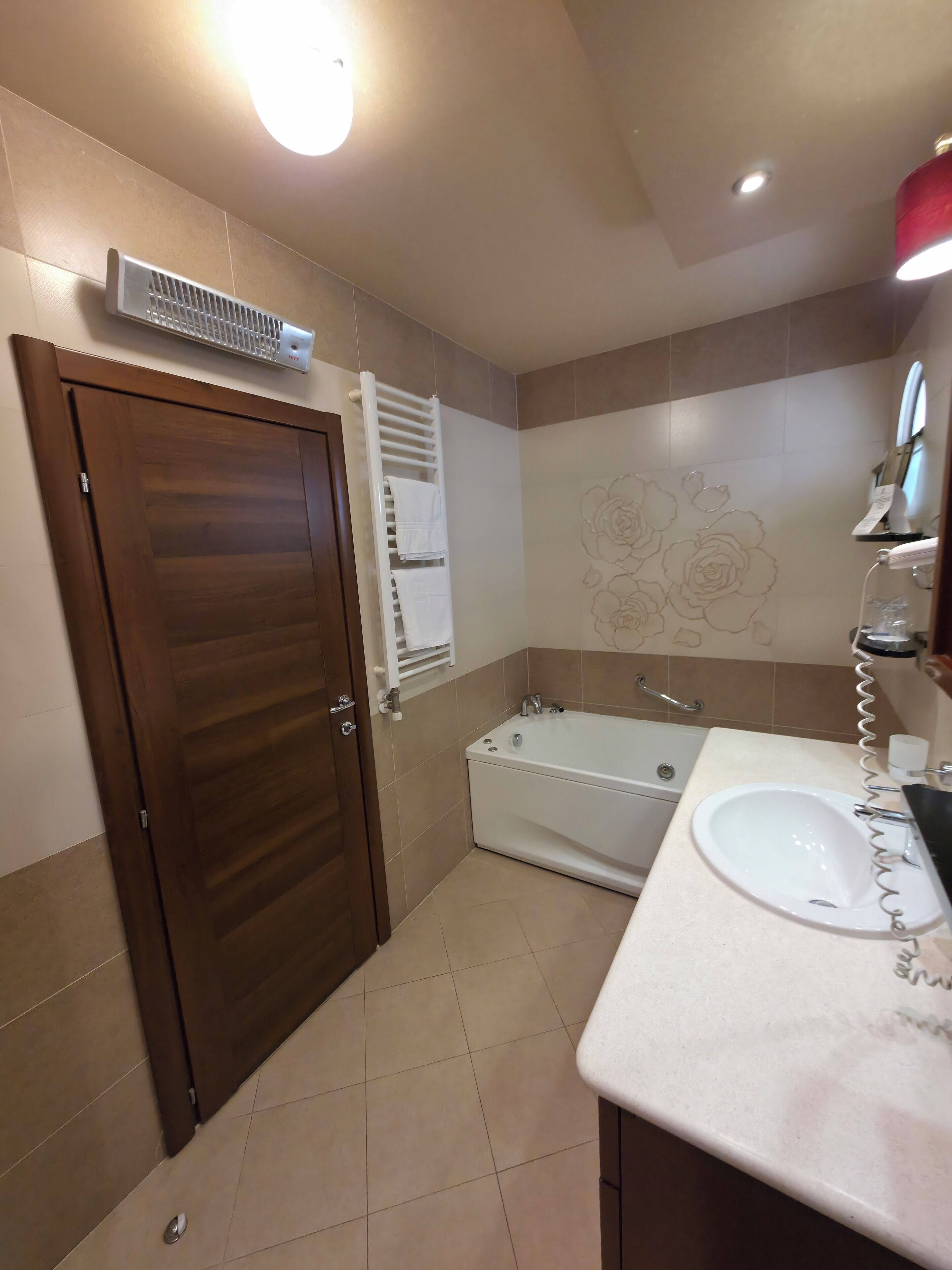 A bathroom with a wooden door, a white bathtub, a sink, and a towel rack.
