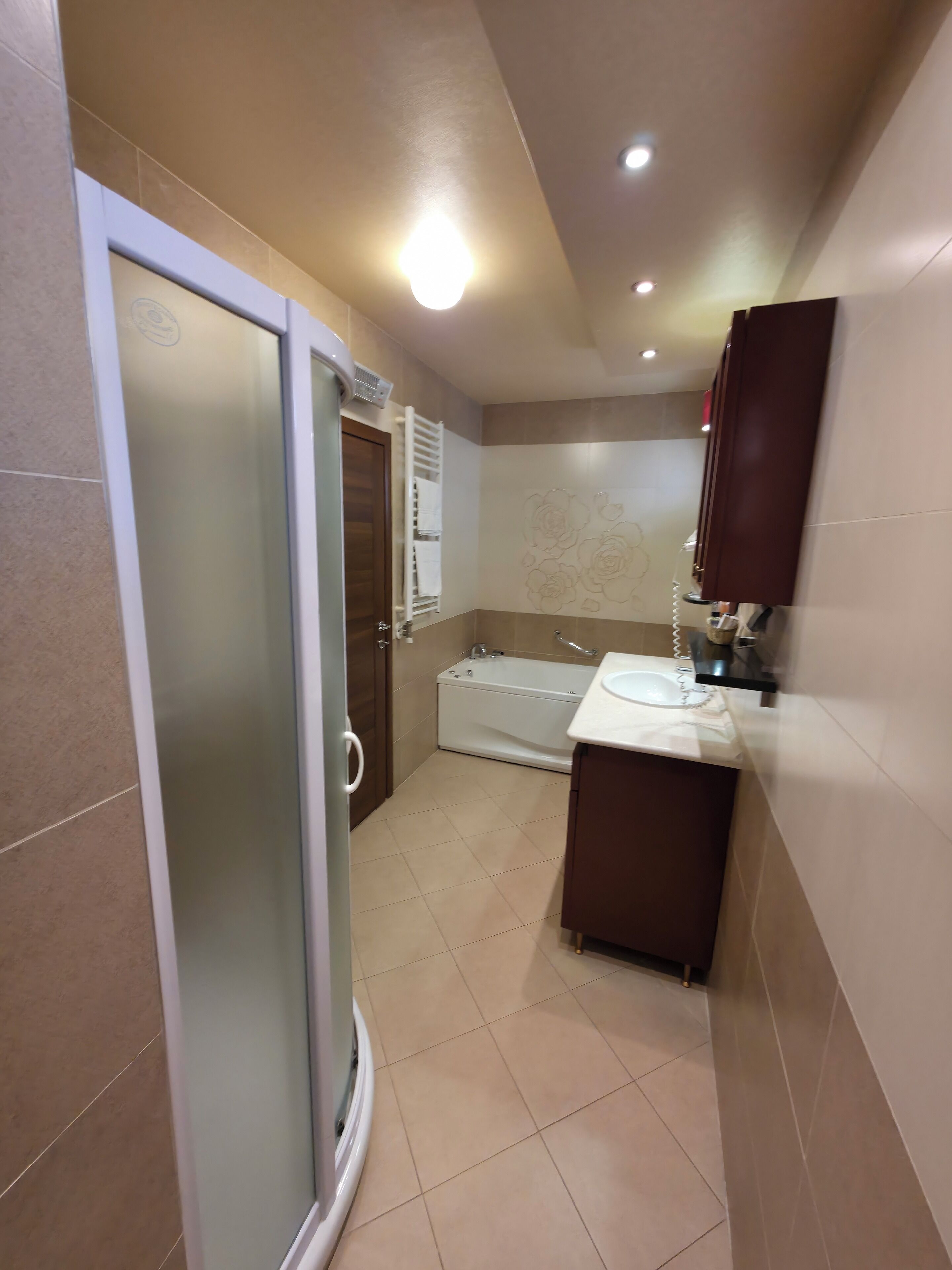 Un baño con mampara de vidrio, bañera y lavamanos con espejo.