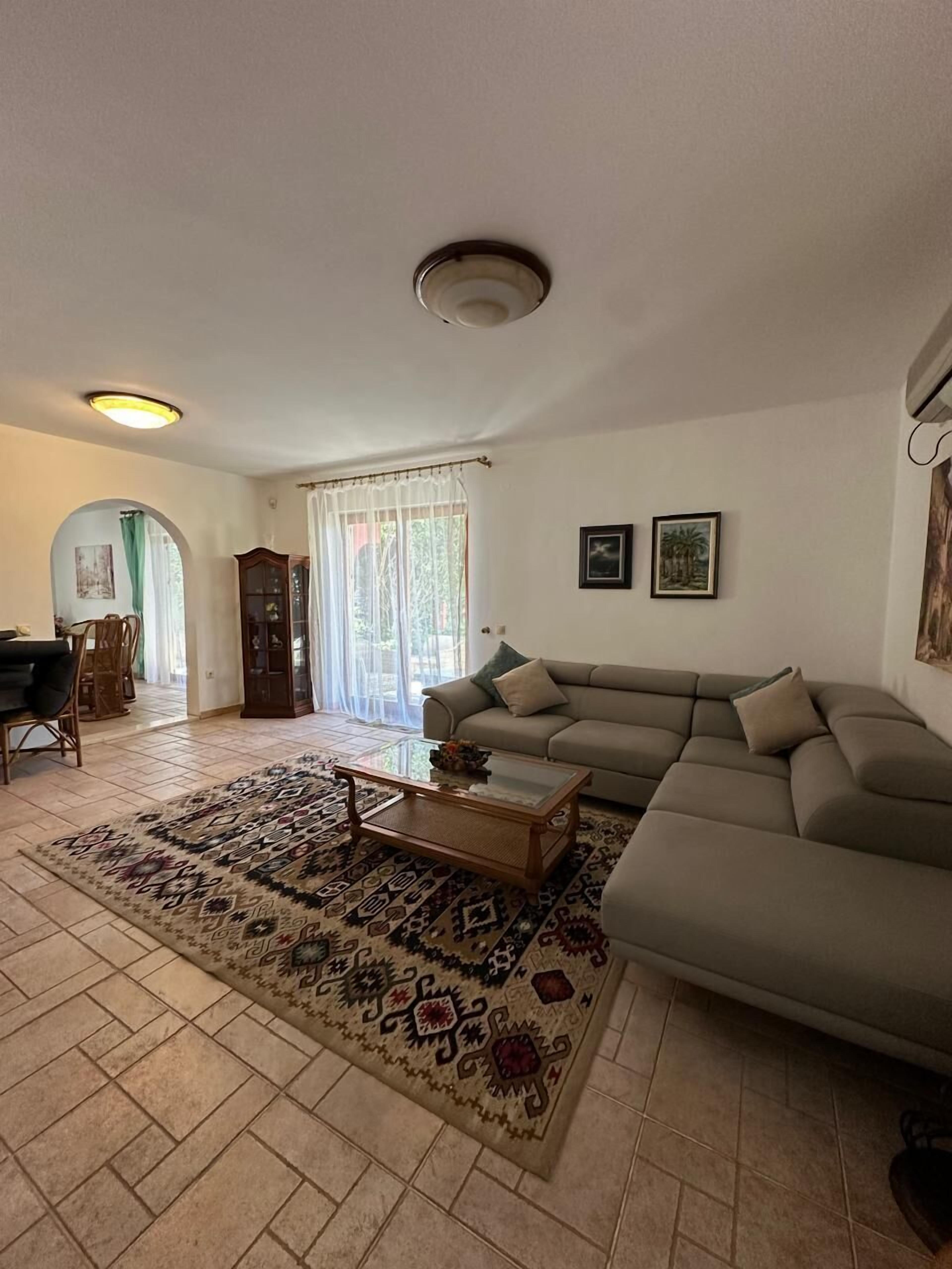 Un salon comprenant un canapé, une table basse, un tapis à motifs, un meuble et une porte donnant sur l’extérieur.
