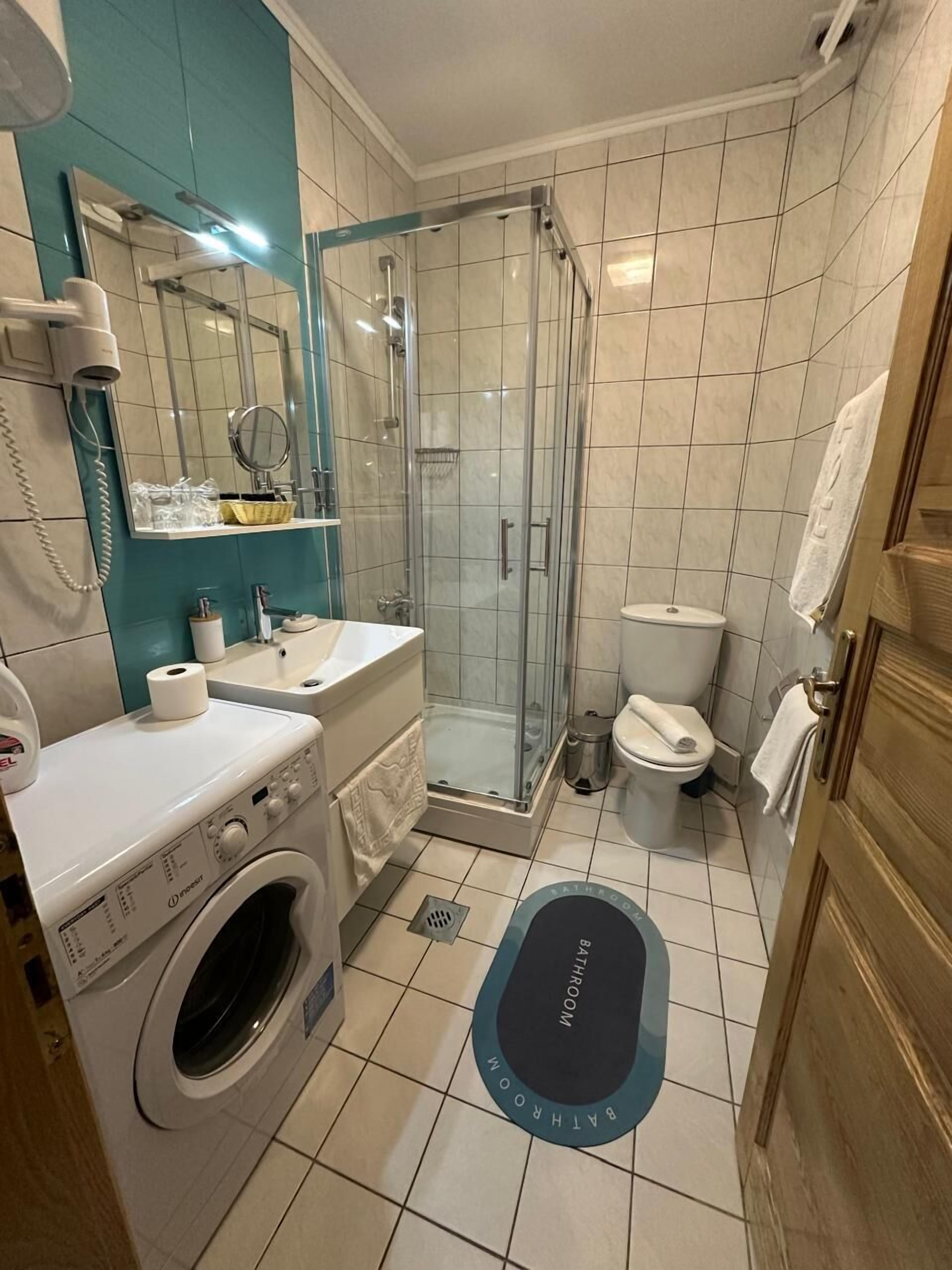 A bathroom with a glass-enclosed shower, a toilet, a sink, and a washing machine.