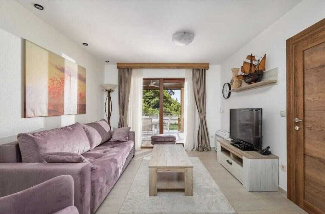 A living room with a sofa, a coffee table, a television on a stand, and a door.