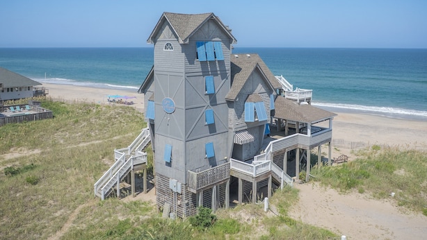 A coastal house with multiple levels, a balcony, and a view of the beach and ocean.