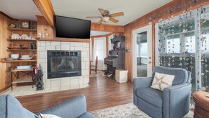 A cozy living room with a fireplace, wooden shelves, a television, and a piano.