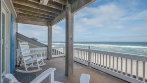 A wooden deck with white rocking chairs overlooking a beach.