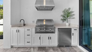A modern outdoor kitchen with a stainless steel range, a built-in sink, and a dishwasher. - 1 Mile to Beach! | Heated Pool | New Construction (Naples)