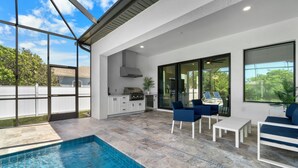 A modern outdoor pool area with a kitchen and seating area. - 1 Mile to Beach! | Heated Pool | New Construction (Naples)