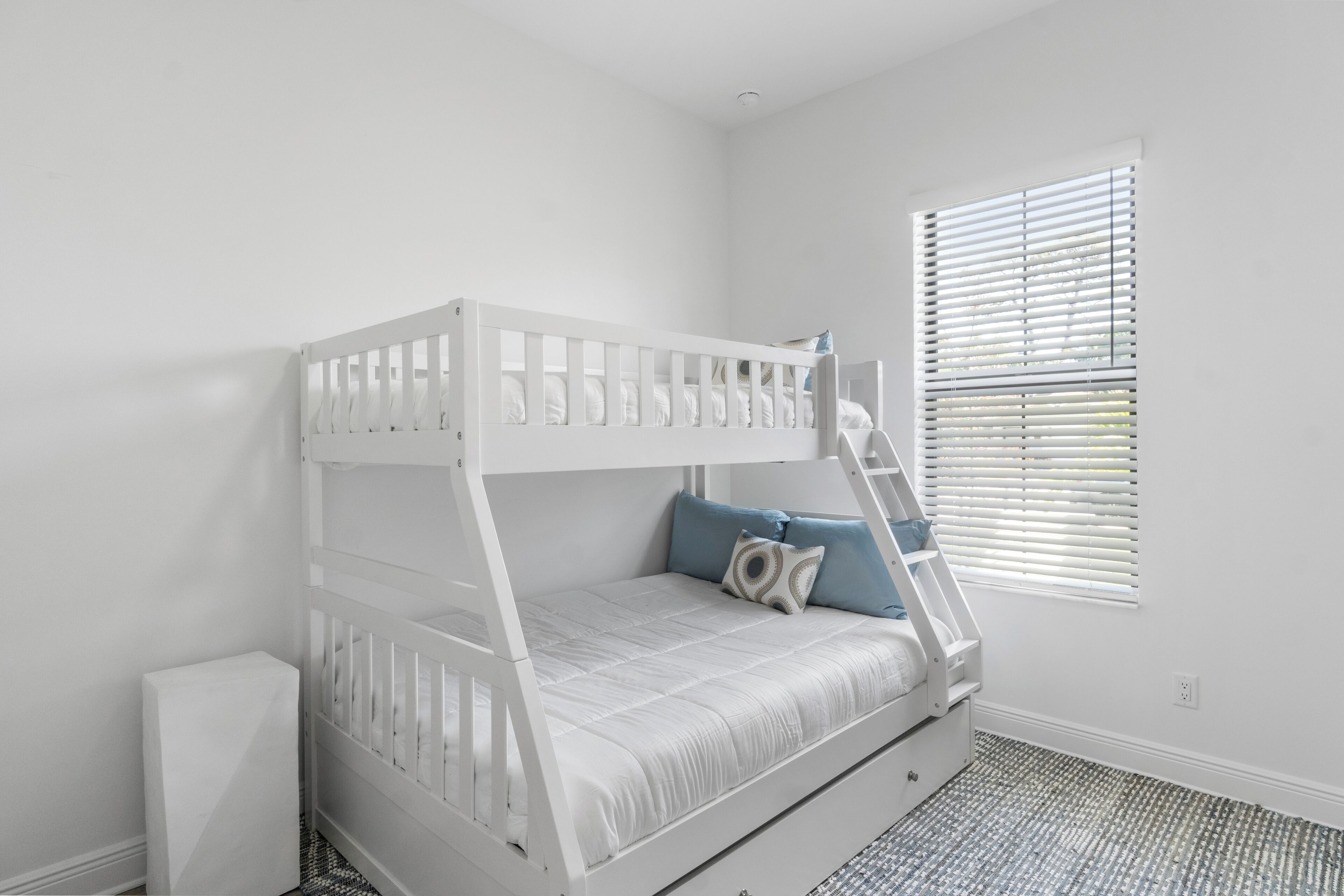 A bunk bed with a ladder, a window with blinds, and a patterned floor.