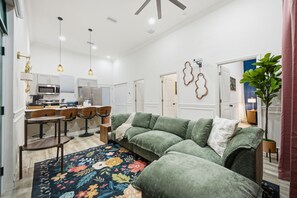 A modern living room with a sectional sofa, a dining area with bar stools, and a kitchen with a microwave.