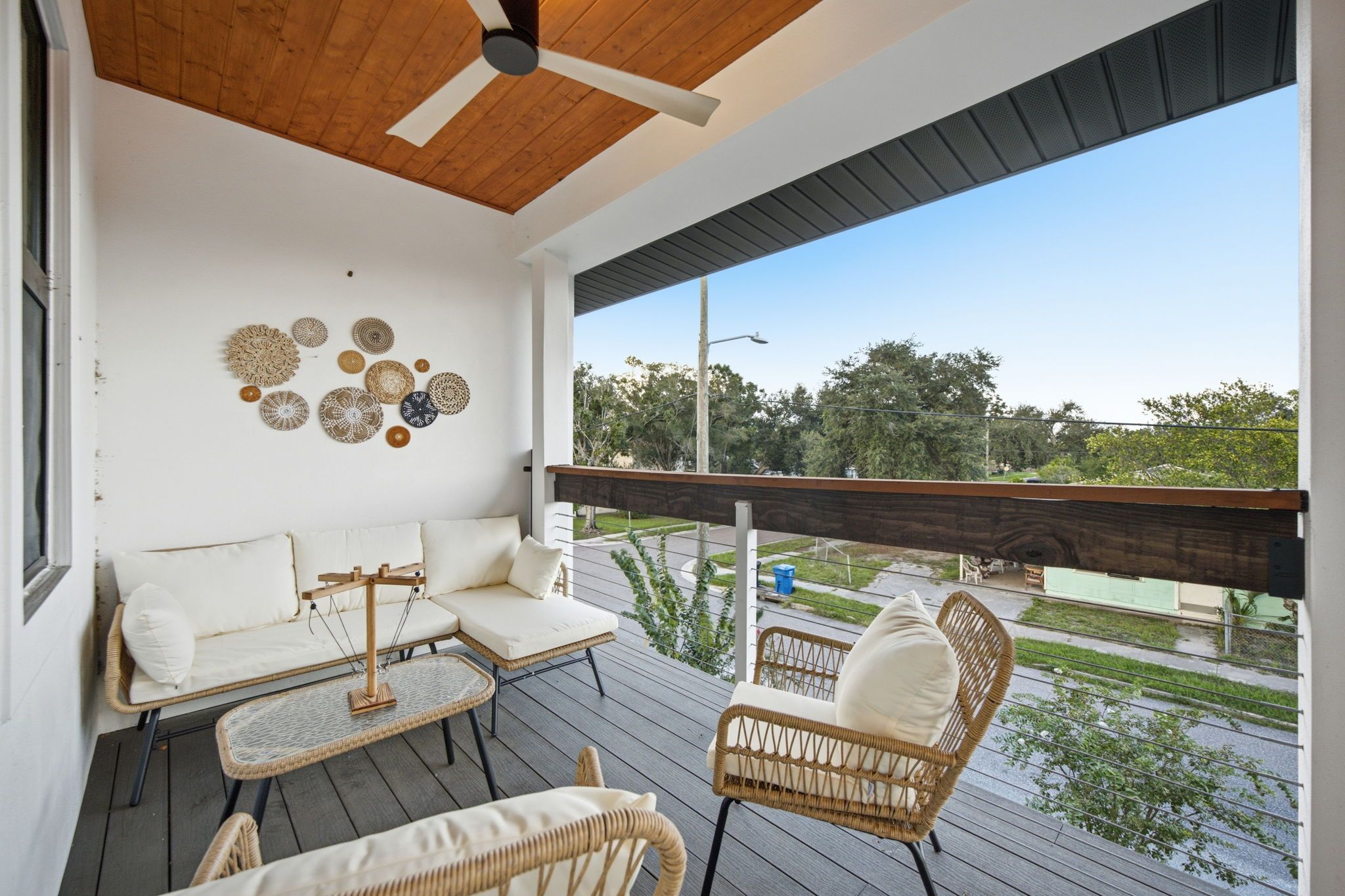 A covered outdoor seating area with wicker furniture, a ceiling fan, and decorative wall art.