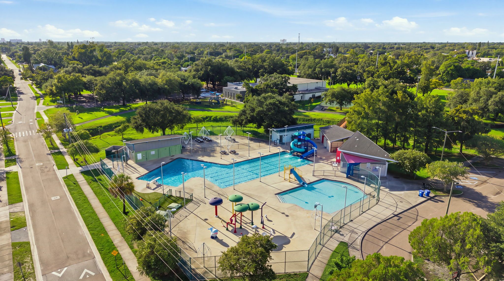 A large outdoor swimming pool with a water slide and a separate smaller pool, surrounded by green lawns and trees.