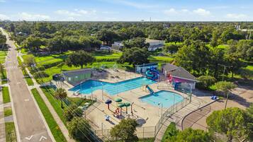 A large outdoor swimming pool with a water slide and a separate smaller pool, surrounded by green lawns and trees.