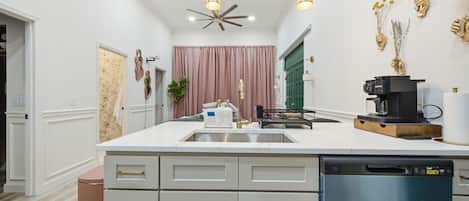 Una cocina moderna con una isla central, armarios blancos, lavavajillas integrado y un ventilador de techo.