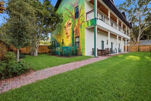 A two-story building with a large mural on the side, a covered patio with outdoor furniture, and a well-maintained lawn.