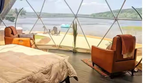 A tented accommodation with a bed, two chairs, and a view of a lake. - Luxury lakefront dome with private beach, close to nature and town! (Lunenburg)