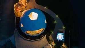 A dome-shaped building with a central skylight, surrounded by a circular pathway and illuminated by string lights. - Luxury lakefront dome with private beach, close to nature and town! (Lunenburg)