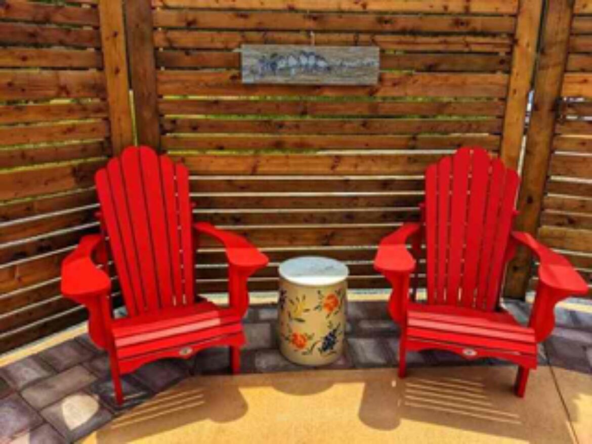 Two red Adirondack chairs facing each other with a small round table between them.