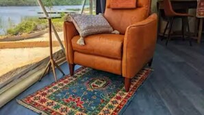 A tent with a view of a lake, a brown leather chair with a pillow, and a colorful rug. - Luxury lakefront dome with private beach, close to nature and town! (Lunenburg)