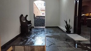 A wet hallway with a bench, a potted plant, and a gate leading to a brighter area. - https://www.airbnb.com.br/hosting/listings/editor/1429156678113976343 (Parque Industrial São José dos Campos)