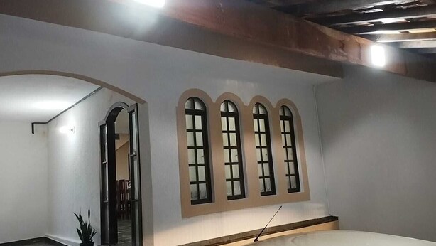 A modern interior with a car parked in a garage. There are three arched windows and a staircase leading to an upper level. - https://www.airbnb.com.br/hosting/listings/editor/1429156678113976343 (Parque Industrial São José dos Campos)