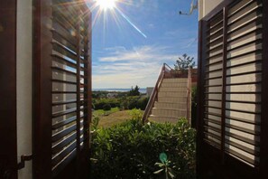 A view through a doorway with a sun shining, a staircase, and a garden with plants.