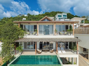 A two-story house with a swimming pool, large windows, and a balcony.