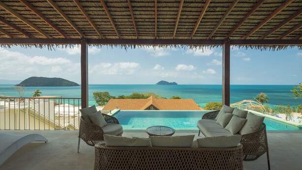 Un espace extérieur aménagé, abrité et doté de mobilier en osier, offrant une vue sur une piscine et une plage tropicale.